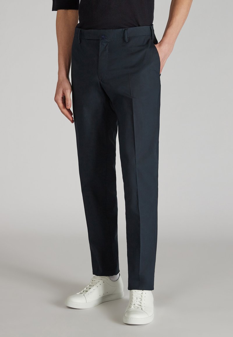 Pantalones azul marino de tela suave, con corte recto, bolsillos delanteros y combinados con zapatillas blancas para un contraste.