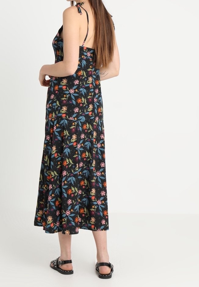 Svart blommig maxiklänning med justerbara spaghettiremmar, har ett färgglatt blommönster och en svängd fåll, tillsammans med svarta sandaler.