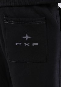 Primer plano de un bolsillo de pantalones negros con un símbolo de estrella gris y el texto "pxp" impreso en la tela, con costuras visibles alrededor del bolsillo.
