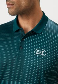 Zöld polóing texturált rácsos mintával, háromgombos gombolással és EA7 Emporio Armani logóval a bal mellen.