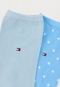 Ζευγάρι από μπλε κάλτσες· η μία μονόχρωμη ανοιχτό μπλε και η άλλη ανοιχτό μπλε με λευκά πουά. Και οι δύο έχουν μια μικρή ετικέτα με λογότυπο στον αστράγαλο.