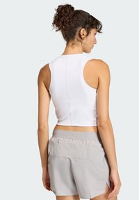 White cropped tank top with a smooth texture, featuring a round neckline and racerback design, paired with light gray shorts.