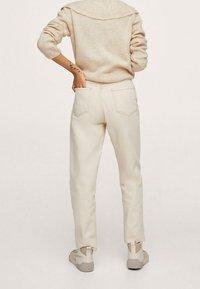 Pull crème avec un col à côtes larges, porté avec un pantalon beige clair fuselé doté de poches arrière et d'ourlets retroussés. Baskets beiges.