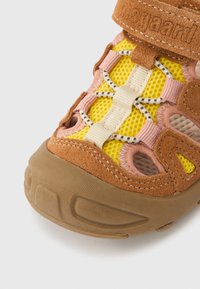 Καφέ σανδάλι από σουέντ και δίχτυ με κίτρινες, ροζ και κρεμ λεπτομέρειες· διαθέτει υφασμένο λάστιχο στη σόλα και ελαστικά κορδόνια για σταθερή εφαρμογή.