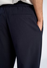 Pantalons bleu marine à taille élastique présentant une texture lisse, des poches latérales et arrière, avec une coupe décontractée et des détails de design minimaux.