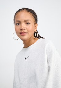 Sudadera gris hecha de una tela suave, con un logo negro de Nike en el pecho. El diseño incluye un escote redondeado y un corte relajado.