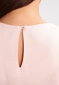 Light pink fabric with a keyhole opening at the back, secured by a fabric-covered button. Texture is smooth and slightly sheer.