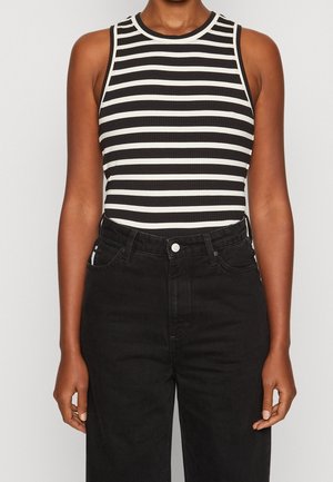 Haut sans manches à rayures noires et blanches avec une texture côtelée. Associé à un jean noir taille haute. Coupe décontractée et design épuré.