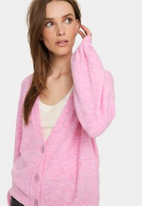 Rosa cardigan i mjukt tyg med v-ringning, långärmar och knapplist fram. Har en subtil texturvariation och rundade manschetter.