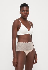 Seno bra wireless bianco con scollatura profonda abbinato a mutandine beige con pizzo e un design a onde con motivo floreale.