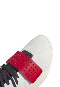 Vit sneaker med en texturerad nätovandel, marinblå snörning och ett iögonfallande röd perforerat rem med svarta detaljer.