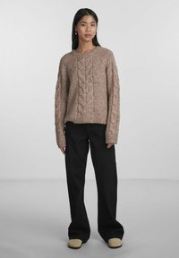 Knit sweater in beige with a textured design, featuring cable-knit patterns. Paired with black wide-leg pants and beige slip-on shoes.