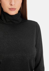Schwarzes Rollkragenoberteil aus einem strukturierten Stoff mit einem leichten Glanz. Enganliegendes Design, lange Ärmel und ein hoher Kragen.