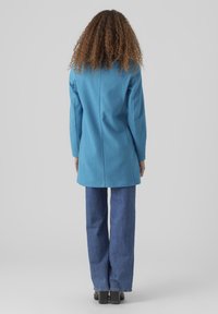 Blå ullrock med en strukturerad silhuett, långa ärmar och en detalj med baksöm, tillsammans med utsvängda denimjeans och klackstövlar.