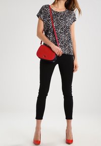 Top s leopardím vzorem v černobílé, černé skinny džíny, červené lodičky na vysokém podpatku a červená kabelka přes rameno s modrým akcentem.