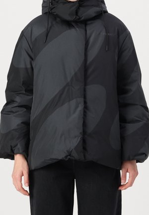 Person wearing a black puffer jacket with abstract dark gray patterns, hood, and elastic cuffs, standing against a plain background.