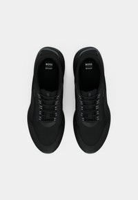 Des chaussures de sport noires en mesh et caoutchouc, présentant une surface texturée, des accents gris et un système de laçage traditionnel.
