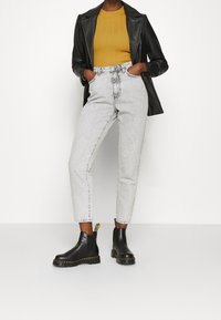 Šedé džíny s vysokým pasem a uvolněným střihem, kombinované s hořčicovým žebrovaným svetrem a černou koženou bundou. K tomu černé chelsea boty.