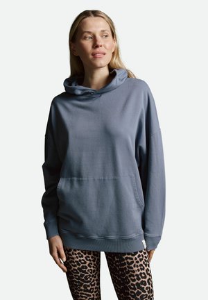 Blaues übergroßes Hoodie mit einer Kordelzugkapuze, Fronttasche und gerippten Bündchen. Kombiniert mit schwarzen Leggings im Leopardenmuster.