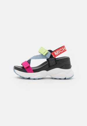Stevige zwart-witte platformsandaal met roze, groene en blauwe bandjes en een rode enkelband met witte tekst.