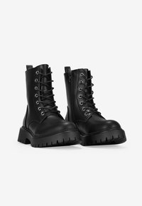 Black lace-up ankle boots made of smooth leather, featuring a chunky sole with treads and decorative stitching along the edges. Zipper closure on one side.