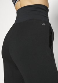 Czarne legginsy o wysokim stanie z szerokim pasem i boczną kieszenią, z małym logo "CK" na biodrze.