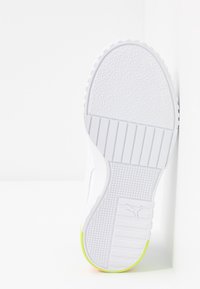 Semelle de chaussure blanche avec motifs texturés antidérapants et logo Puma sur la zone du talon, montrant les détails de la bande de roulement et un bord légèrement jaune néon.