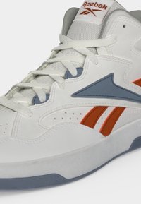 Λευκό ψηλό αθλητικό παπούτσι Reebok με μπλε και πορτοκαλί λεπτομέρειες και λευκά κορδόνια σε λευκό φόντο.