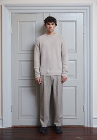 Jersey de punto texturizado color beige claro con cuello redondo, combinado con pantalones sueltos color gris claro. Footwear negro completa el aspecto.