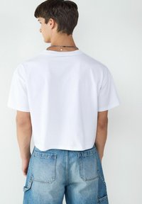 Biała bawełniana koszulka o luźnym kroju i krótkich rękawach, charakteryzująca się gładką fakturą. Nosi się ją z jasnoniebieskimi dżinsowymi spodniami cargo z dużymi kieszeniami.