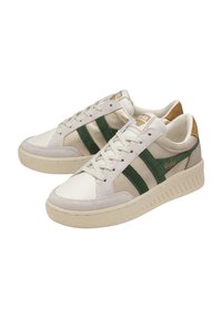 Sneakers bianchi con strisce in suede verde e un accento in pelle beige. Presentano una suola in gomma testurizzata e dettagli cuciti. Logo dorato sulla linguetta.