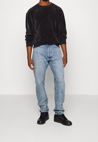 Svart sammetströja med ribbade ärmslut och halsringning, tillsammans med ljusblå jeans i en avslappnad passform och blekt utseende. Svarta sneakers.