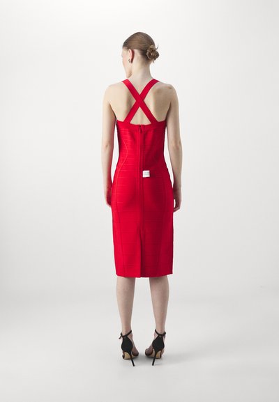 Abito rosso aderente con spalline incrociate e motivo testurizzato, lungo fino al ginocchio, chiusura con cerniera sul retro, abbinato a scarpe nere con tacco alto.