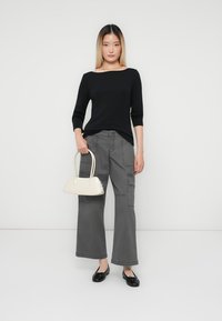 Zwarte lange mouw top gecombineerd met grijze cargobroek met zakken, en een witte handtas. Zwarte platte schoenen maken de look compleet.