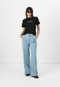 Zwarte katoenen t-shirt met witte "Calvin Klein" logo, gecombineerd met lichtblauwe wijde denim jeans en zwarte schoenen. Glad textuur en casual pasvorm.