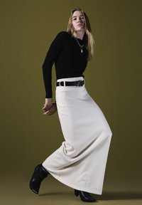 Zwarte geribbelde langemouwen top gecombineerd met een high-waisted crèmekleurige maxi rok. Accessoires zijn onder andere een zwarte riem en een gelaagde zilveren ketting. Zwarte enkellaarsjes.