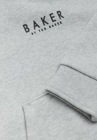 Siva sweatshirt iz mehkega blaga, z rebrastimi manšetami in s črnim napisom "BAKER BY TED BAKER" na prsih.