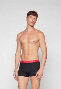 Caleçons boxers noirs avec une ceinture élastique rouge arborant le logo "PUMA". Le tissu semble lisse avec un ajustement confortable et une longueur moyenne.