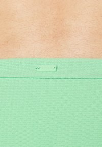 Zöld mintás anyag, texturált felülettel, egy kis Roxy címkével. A dizájn rácsszerű mintát és sima derékrészt tartalmaz.