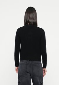 Svart strikkegenser med lange ermer og rund hals, kombinert med mørkegrå cargobukser. Strukturert stoff og tettsittende design.