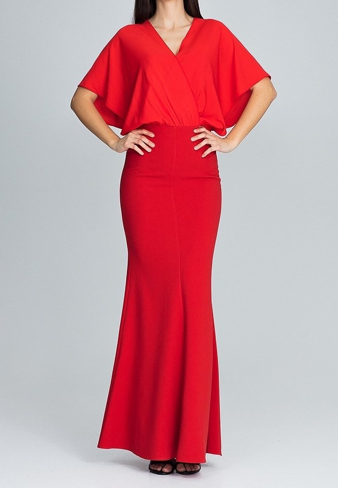 Femme portant une robe rouge longue jusqu'au sol avec un profond décolleté en V et des manches larges, les mains posées sur les hanches, debout devant un fond uni.