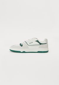 Hvit sneakers med grønne detaljer, laget av lær og semsket skinn. Har en teksturert tunge, flate snørebånd og en tykk gummisåle.