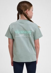 Jasnozielona bawełniana koszulka z okrągłym dekoltem i krótkimi rękawami, z nadrukowanym logo na plecach w kolorze miętowym i białym.