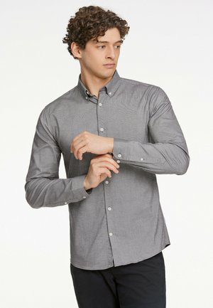 Camisa gris de manga larga con un patrón texturizado. Presenta un cuello abotonado y puños abotonados. Se lleva con pantalones oscuros.