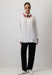 Wit overhemd met knopen en een kraag geïnspireerd op rode koraal, gecombineerd met zwarte, loszittende broek en witte sneakers. Gladde stoftextuur.