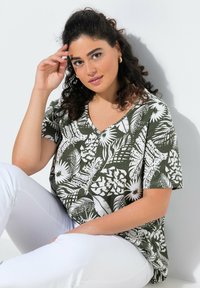 Zelený a bílý vrchní top s krátkým rukávem a výstřihem do V, s tropickým vzorem listů, uvolněný střih, nošený s bílými kalhotami, texturovaná tkanina.