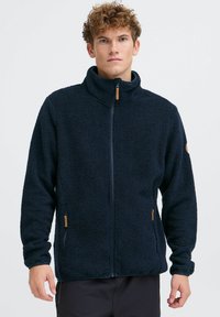 Marineblaue Fleecejacke mit hohem Kragen, durchgehendem Reißverschluss und Seitentaschen. Verfügt über einen strukturierten Stoff und einen Reißverschluss-Zipper mit Holzakzent.