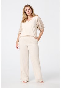 Beige top met een V-hals en textuurpuffmouwen, gecombineerd met lichtbeige broek met wijde pijpen en zijsplitten. Glad materiaal, relaxte pasvorm.