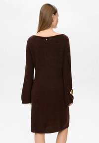 Rochie tricotată de culoare ciocolatie, cu mâneci lungi, în formă de clopot, un decolteu larg și un detaliu cu nasturi la spate. Textură moale și croială lejeră.