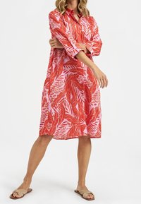 Red and pink leaf-patterned shirt dress with long sleeves, button-down collar, and loose fit, paired with tan flat sandals.